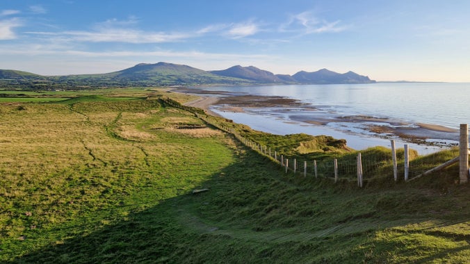 Yr olygfa o fryngaer Dinas Dinlle, Pen Llŷn, gyda llwybr arfordir Cymru yn rhedeg wrth ymyl y traeth a mynyddoedd Yr Eifl yn y pellter.